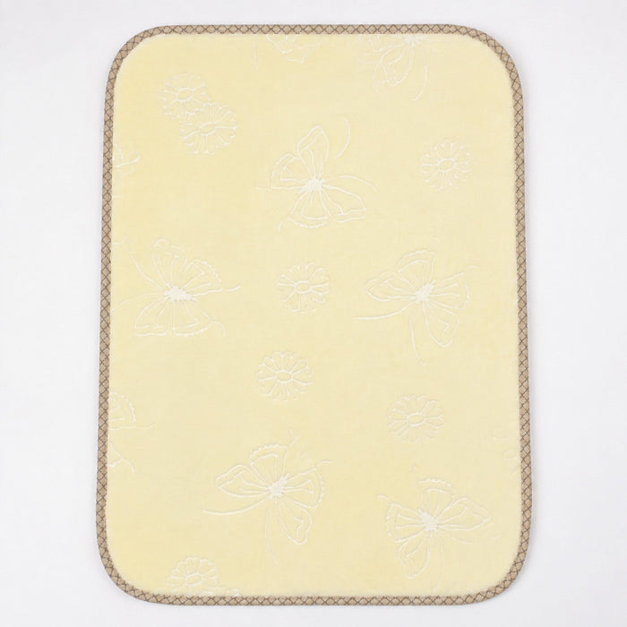 A pale yellow rectangular mat with rounded corners, featuring a subtle white embroidered butterfly and floral pattern and a braided tan border, shown on a plain white background.