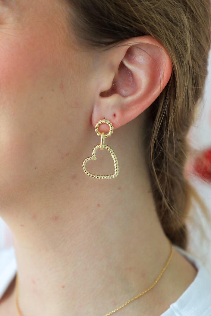 Gold heart-shaped earring worn by a person with a blurred background