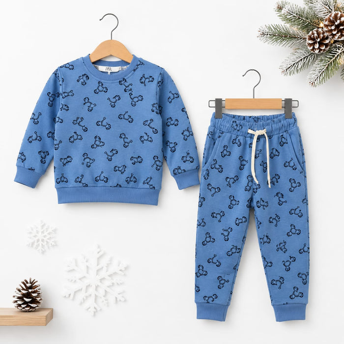 A children's two-piece outfit set featuring a long-sleeve sweatshirt and matching jogger pants in a medium blue color, both printed with a repeating black bow-tie motif. The sweatshirt is shown on a wooden hanger, and the pants are shown on a metal hanger