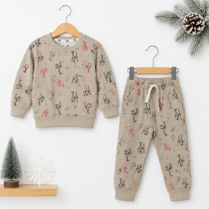 A children's two-piece pajama set consisting of a long-sleeve sweatshirt and matching jogger pants, displayed on wooden hangers against a white background with small holiday props including a pine branch, pinecone, miniature tree, and snowflake.