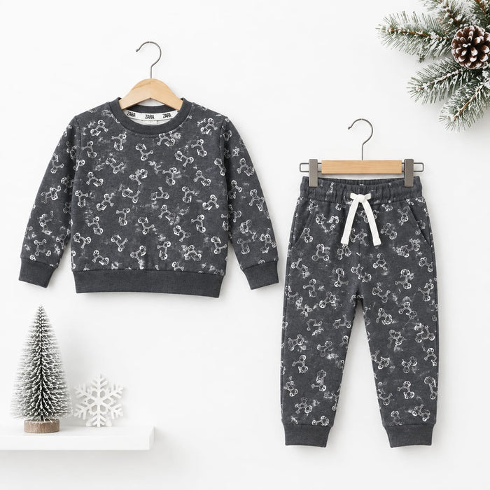 A children's two-piece outfit set consisting of a long-sleeve crewneck sweatshirt and matching jogger pants, both in dark gray with a white snowman pattern, hanging on wooden hangers against a white wall with holiday decorations.