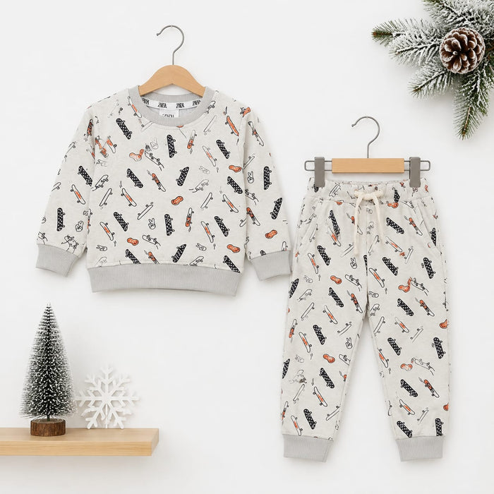 A children's two-piece clothing set featuring a long-sleeve sweatshirt and matching jogger pants, both in a warm off-white color with a playful print of black and orange winter-themed illustrations. The set is displayed on wooden hangers against a clean w