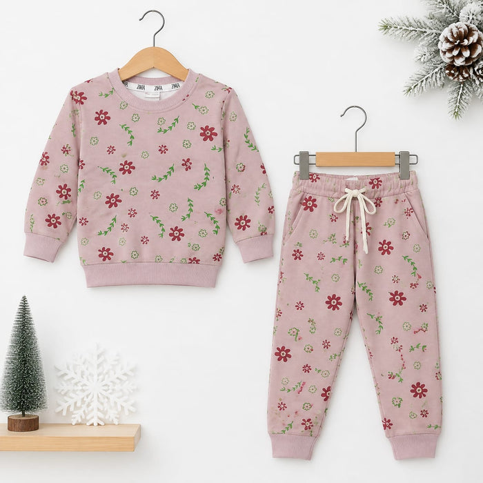 A children's two-piece pajama set hanging on wooden hangers against a white wall. The set includes a long-sleeve sweatshirt and matching jogger pants in dusty pink, both printed with a small red and green floral pattern.