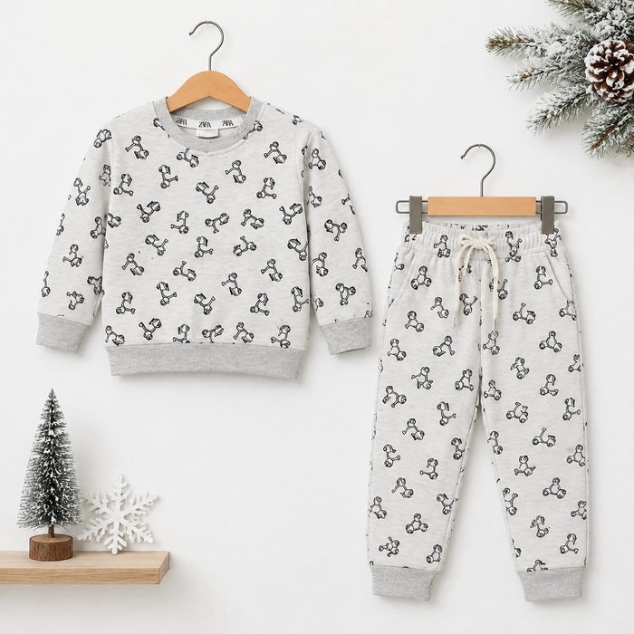 A children's two-piece pajama set hanging on wooden hangers against a white wall. The set includes a long-sleeve sweatshirt and matching jogger pants in a light gray fabric with a black repeating graphic pattern, styled with small holiday props including