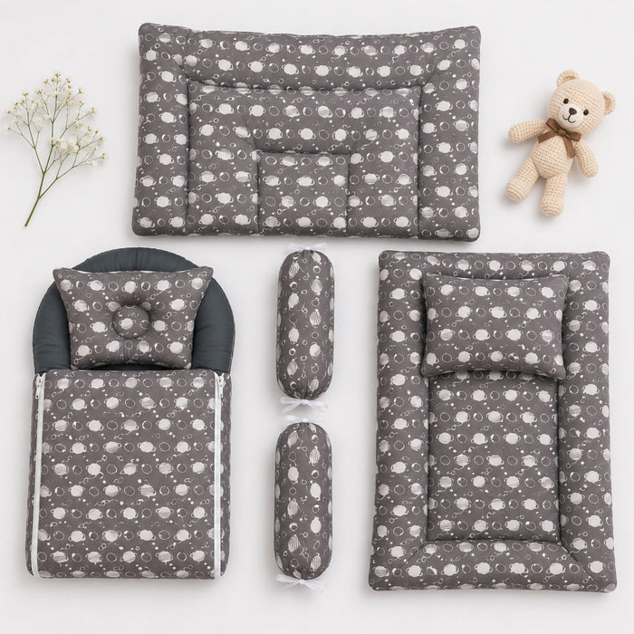 A baby bedding set arranged on a white background, including a changing pad, mattress, footmuff, two cylindrical bolsters, and a matching pillow, all in a gray fabric with a white cloud pattern. A small teddy bear and baby's breath sprig are placed as sty