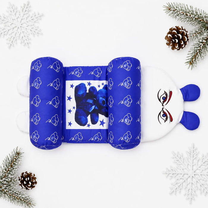 A plush baby support pillow styled in a flat lay with winter-themed props like pine branches, pinecones, and white snowflakes on a white background. The pillow features a blue and white cloud pattern on the sides, a central blue bear graphic, and a white