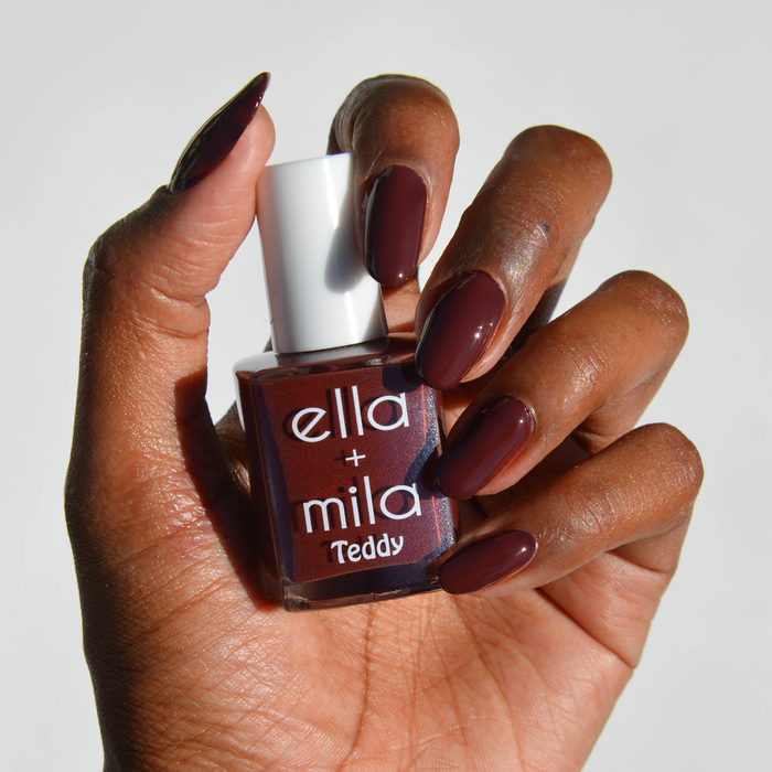Teddy Collection deep red brown nail polish on a deep skin tone, hand holding the bottle