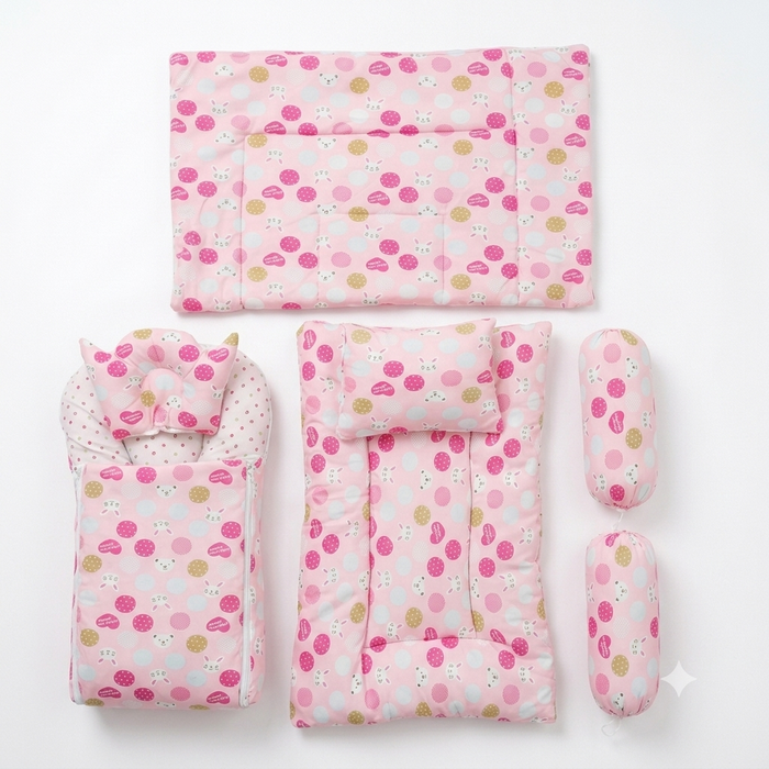 A baby bedding set laid out on a white background, including a quilted mattress protector, a changing pad with a matching pillow, a bassinet cover with a matching pillow, and two cylindrical cushion protectors. The fabric has a light pink base with a patt