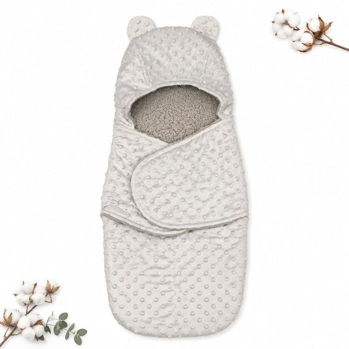 A baby footmuff in a light oatmeal gray color, featuring a textured minky dot pattern on the exterior and a soft, plush fleece lining visible at the opening. The footmuff is styled flat-lay with decorative cotton bolls on a clean white background.