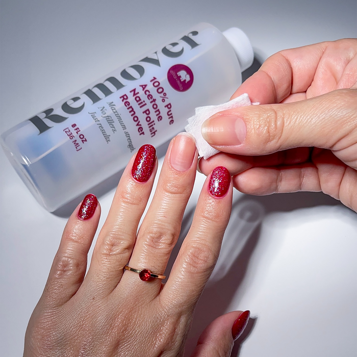 100% Pure Acetone Nail Polish Remover bottle with a burgundy manicure and a cotton pad