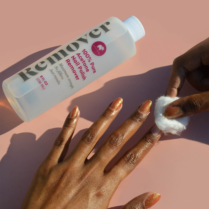 Removing polish with a cotton pad beside the Pure Acetone Remover bottle on a deep skin tone