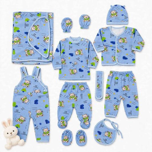 A baby clothing set laid out on a white background, including a light blue long-sleeve top, matching pants, bib, hat, booties, swaddle, and overalls, all printed with a playful cartoon bear and cloud pattern. A small white plush bunny is placed at the low