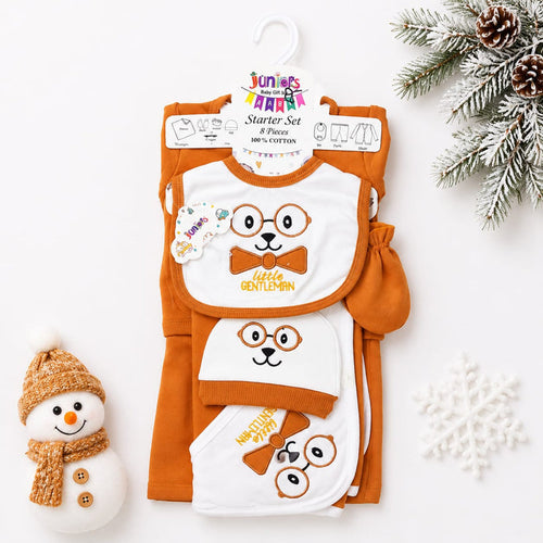 A baby starter set featuring an orange and white knit outfit with matching bibs and a small mitt, displayed on a hanger against a white background with holiday props including a snowman, pine branches, and a snowflake.
