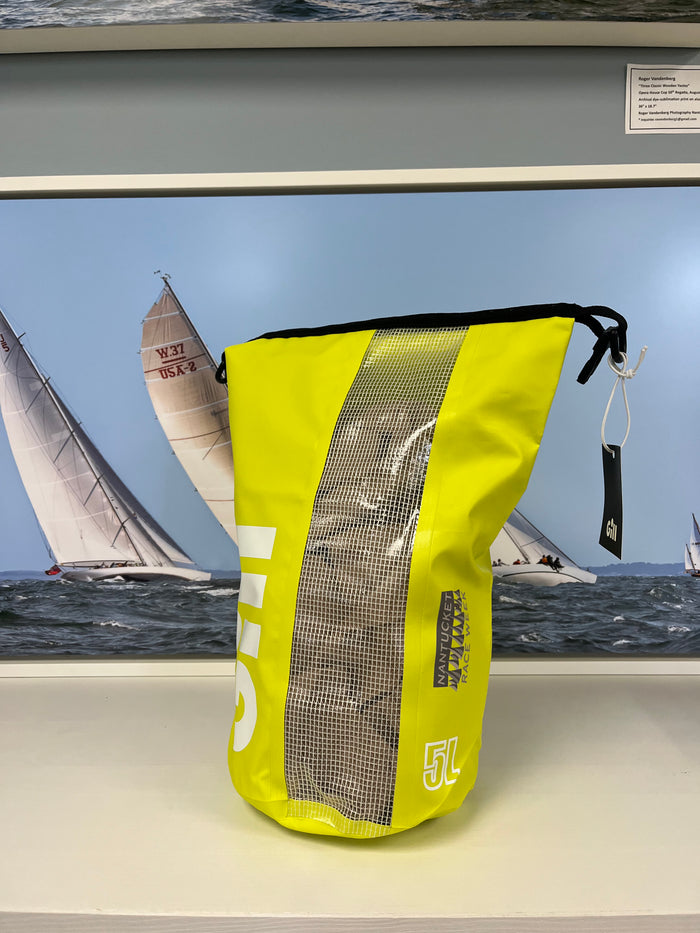 Yellow dry bag with mesh side on a shelf in front of a sailboat picture