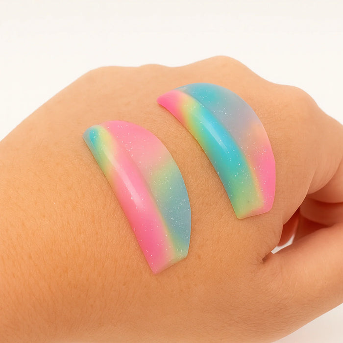Colorful rainbow-shaped gel eyelash lifting shields on a hand against a white background