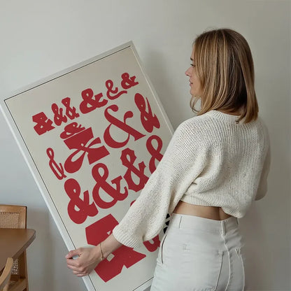 Woman holding a framed "Ampersands Colour Typography Print" with red ampersands on a cream background.