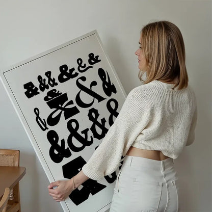 Woman holding a large white typographic print with various black ampersand symbols.