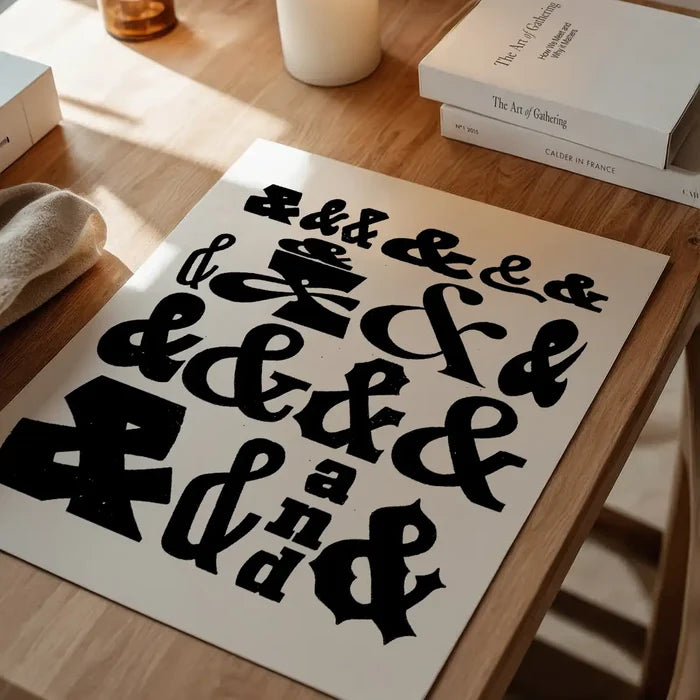 Black ampersands typography print on thick archival art paper, displayed on a light wooden table.