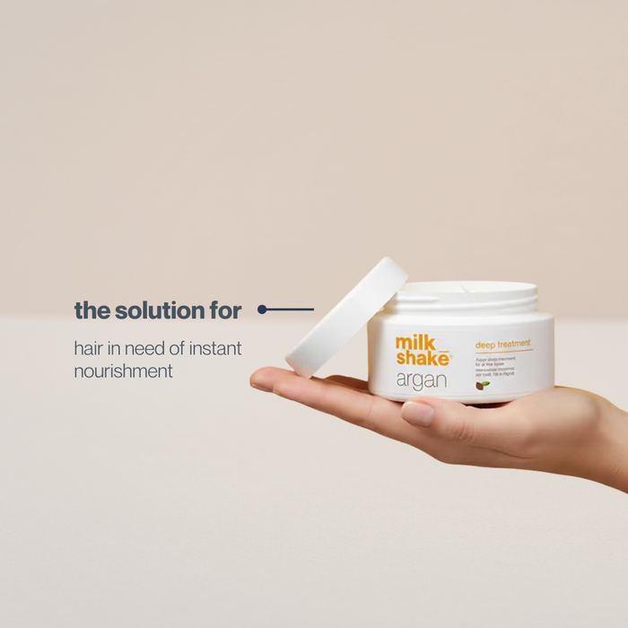 Hand holding a jar of milk_shake Argan deep treatment with text on a beige background