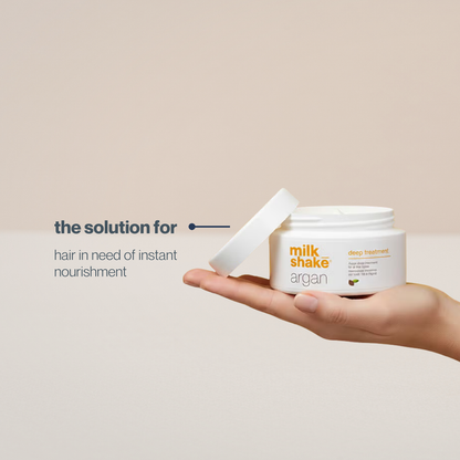 Hand holding a jar of milk_shake Argan deep treatment with text on a beige background
