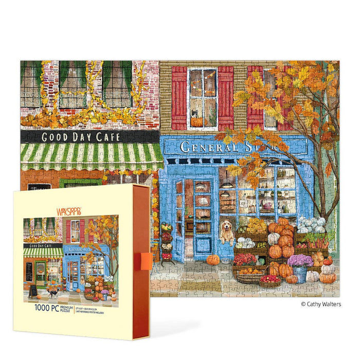 The WerkShoppe "Autumn On Main" 1,000-piece jigsaw puzzle features a fall street scene with a cafe, general store, vibrant autumn trees, pumpkins, and a dog in the shop window. The puzzle box appears prominently in the foreground.