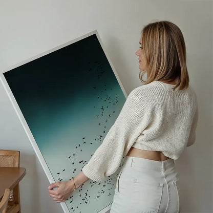 Woman holding a large Scandinavian style "Birds In Flight" print with a dark teal to light blue gradient and black bird silhouettes.