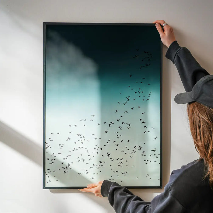 Scandinavian style Birds In Flight print with a flock of black birds against a teal and white sky, held by hands.