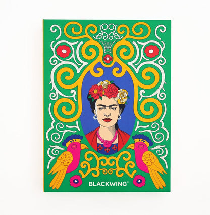 A colorful gift set box featuring a stylized portrait of Frida Kahlo framed by ornate yellow and white swirls on a green background, with two pink and orange birds and the text BLACKWING at the bottom, shown against a plain white background.