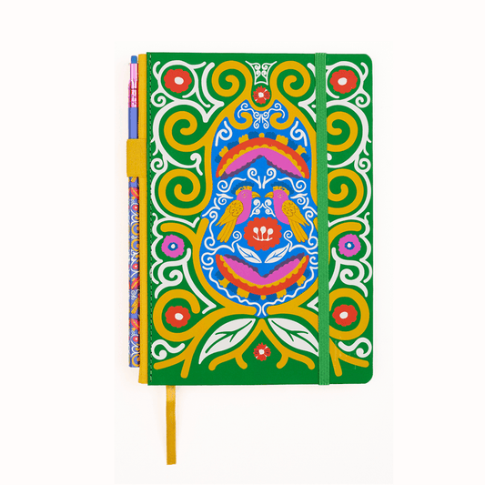 A hardcover notebook with a vibrant green cover decorated with a colorful Frida Kahlo spiral, bird, and floral illustration, featuring a green elastic closure band and a yellow bookmark ribbon with a matching pencil in the pencil holster.