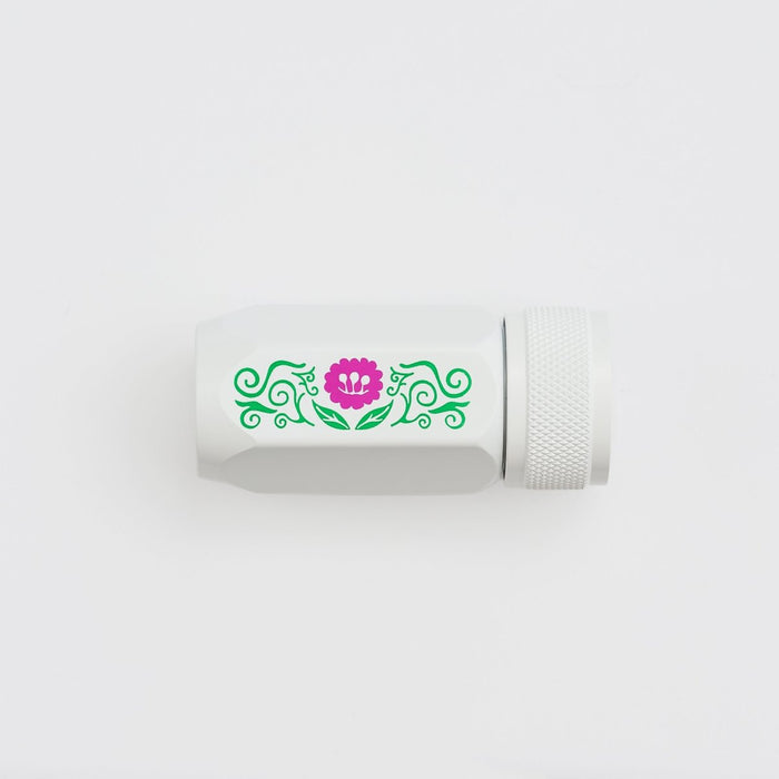 A white cylindrical pencil sharpener with a textured screw-on cap, featuring a decorative green scroll pattern and a pink flower graphic on the side, set against a plain white background.