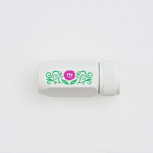 A white cylindrical pencil sharpener with a textured screw-on cap, featuring a decorative green scroll pattern and a pink flower graphic on the side, set against a plain white background.