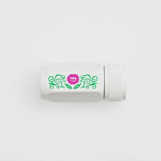 A white cylindrical pencil sharpener with a textured screw-on cap, featuring a decorative green scroll pattern and a pink flower graphic on the side, set against a plain white background.