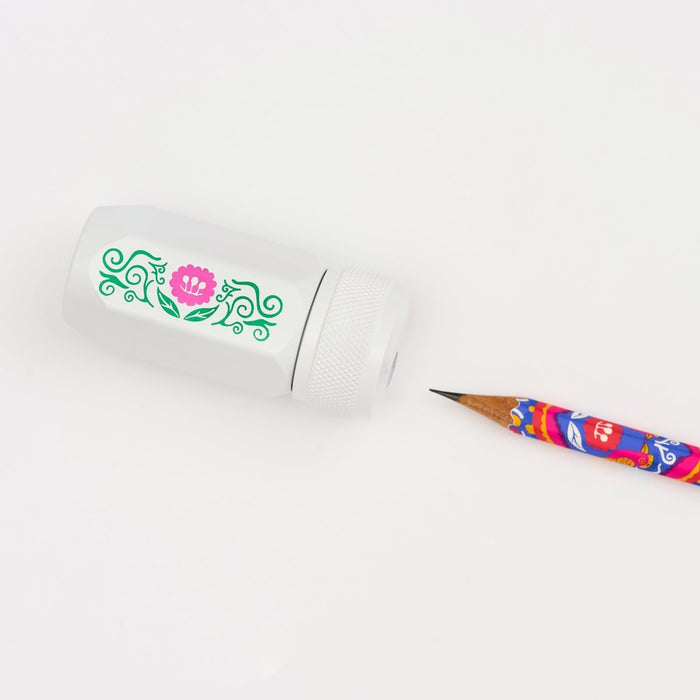 A white pencil sharpener with a green and pink floral design, shown next to a colorful pencil on a clean white background.