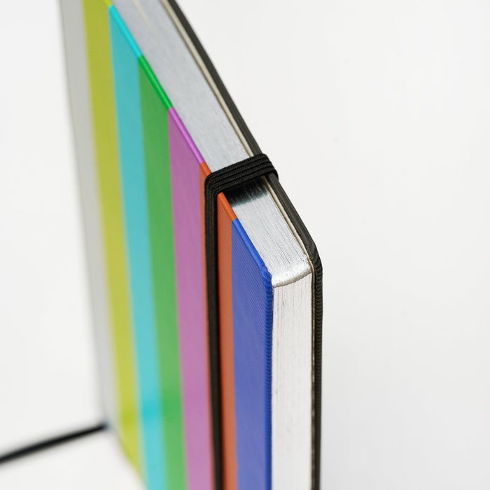 Close-up of a notebook with colorful cover and a black elastic band keeping it closed on a white background