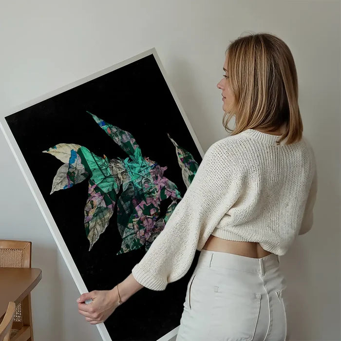Woman holding a large "Botanical 4 Black Print" with layered green and purple leaves on a black background.