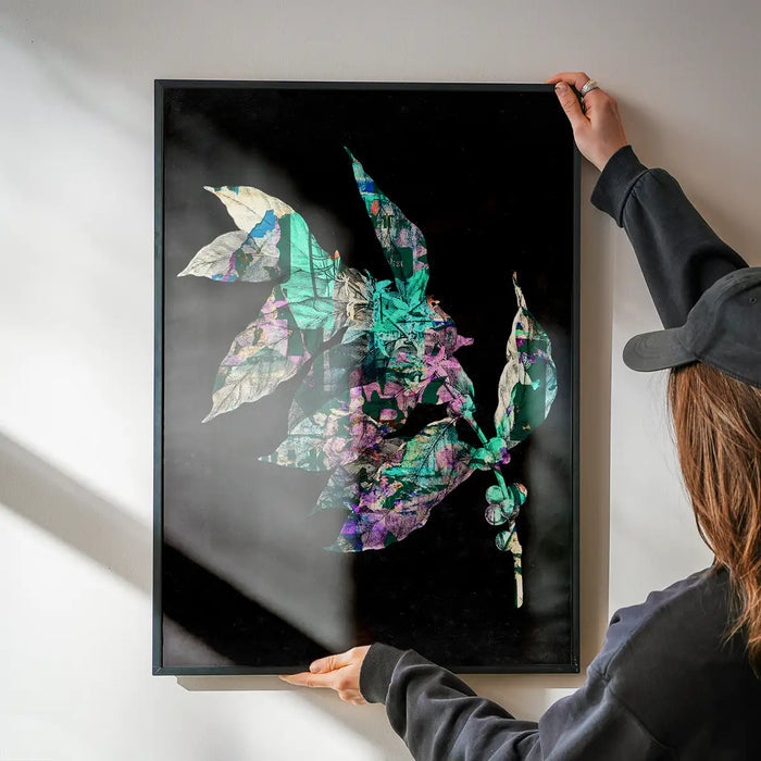 Framed Botanical 4 Black Print with vibrant green and purple layered leaves on a dark background, being hung.