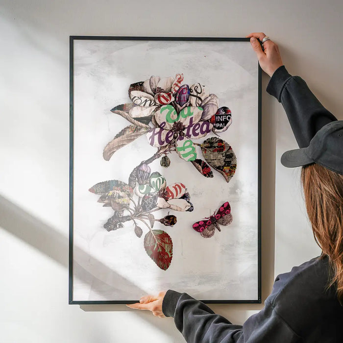 Framed Botanical 7 floral typography print with a pink butterfly, held by hands on a white wall.