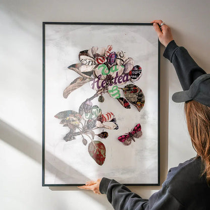 Framed Botanical 7 floral typography print with a pink butterfly, held by hands on a white wall.