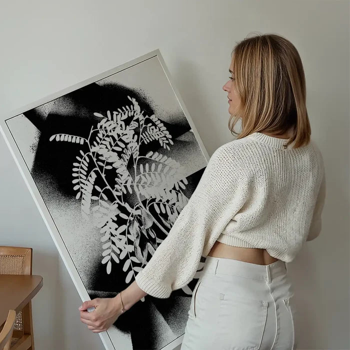 Woman holding a framed Botanical 8 Floral Spray Print with black spraypaint stencil marks and white leaves.