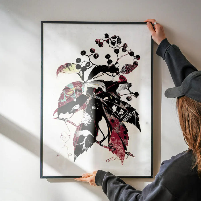 Person holding a framed botanical print with dark leaves, berries, and graffiti art details.