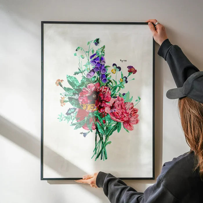 Framed botanical street art print with vibrant pink, purple, and green flowers, held against a white wall.