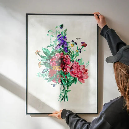 Framed botanical street art print with vibrant pink, purple, and green flowers, held against a white wall.