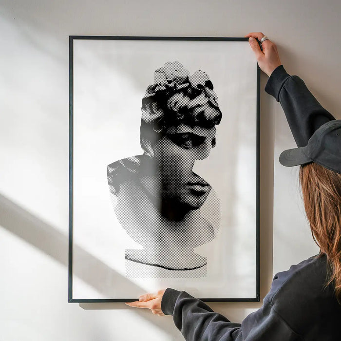 Black and white graphic print of a classic Roman bust, framed, held against a white wall.
