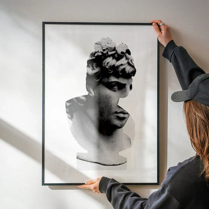 Black and white graphic print of a classic Roman bust, framed, held against a white wall.