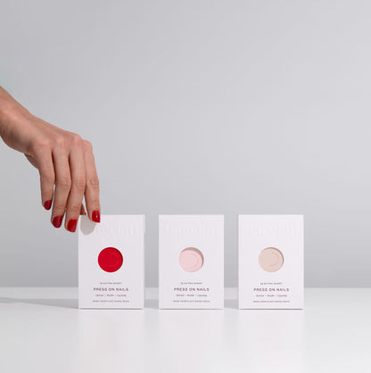 Three boxes of press-on nails held by a hand with red nails