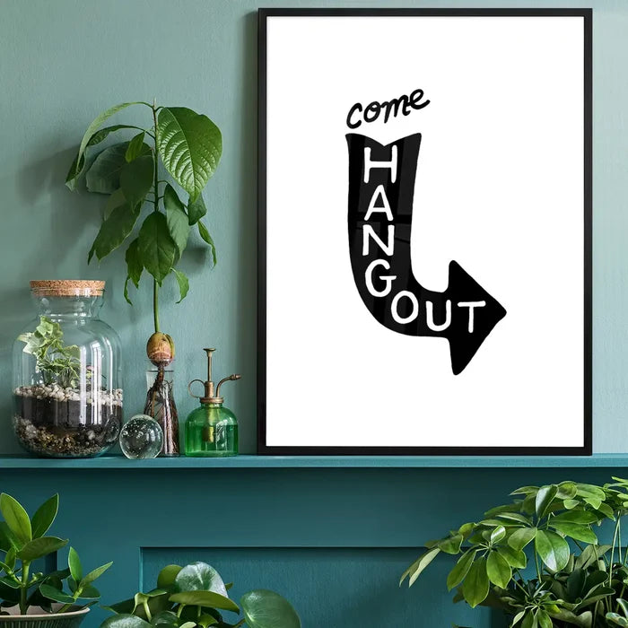 Black framed "Come Hang Out" typographic print on white archival paper, styled on a teal shelf.