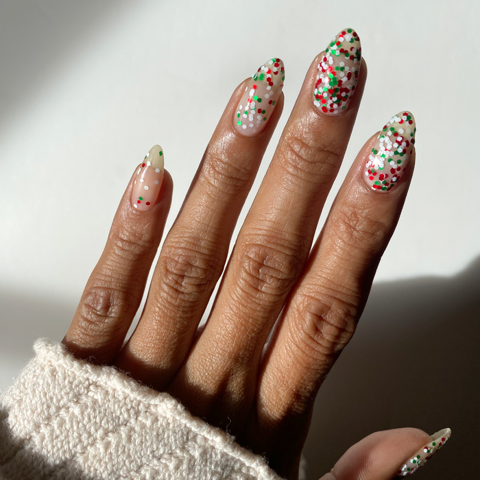 Confetti Cheer red and green confetti glitter over nude nails on a medium skin tone