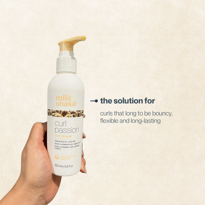 Hand holding a bottle of milk_shake Curl Passion product against a beige background