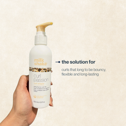Hand holding a bottle of milk_shake Curl Passion product against a beige background