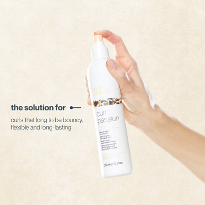 Hand holding a bottle of milk_shake  'curl passion' product against a beige background